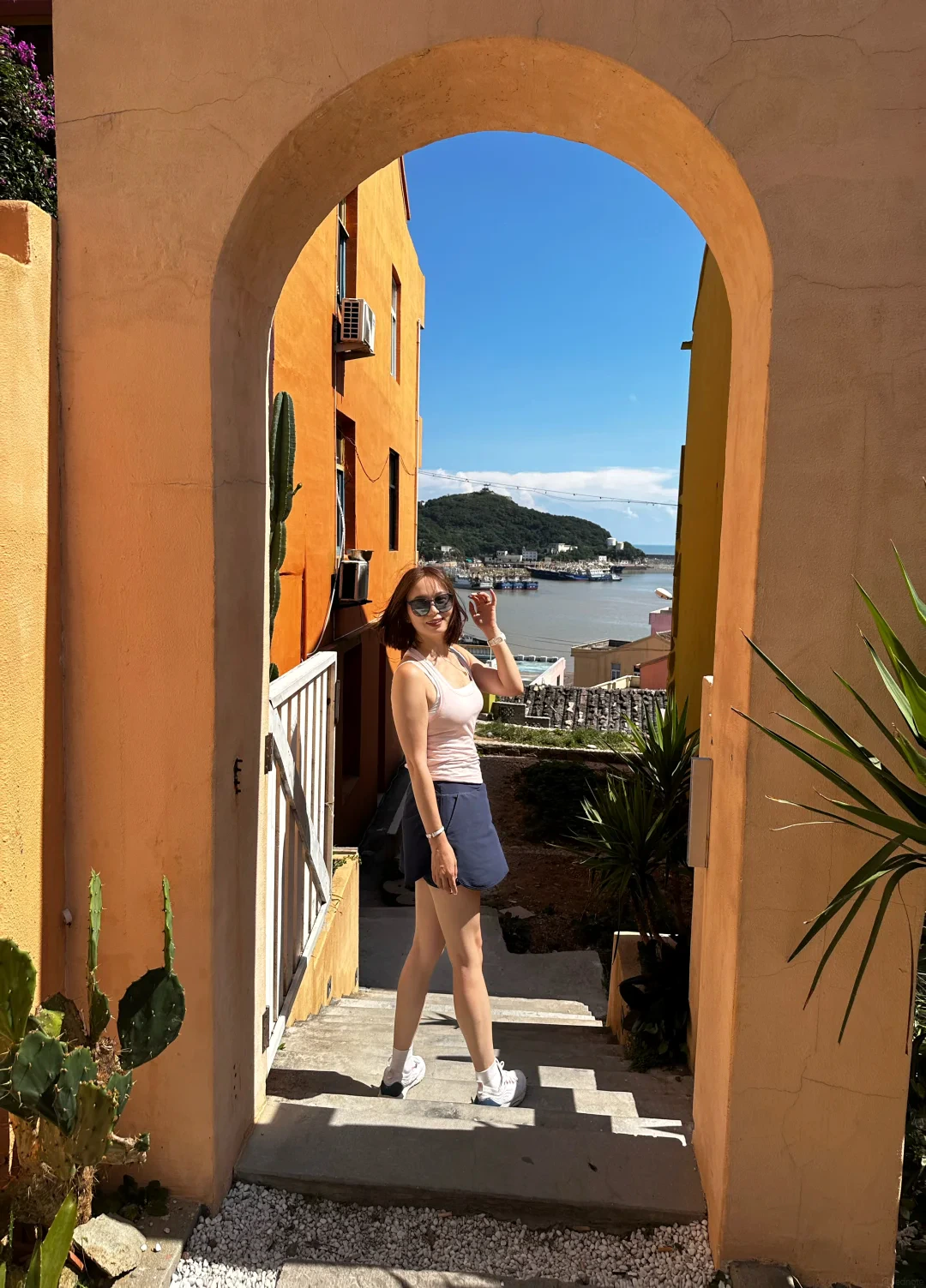 Alicia framed by a sunlit ochre arch above a coastal village