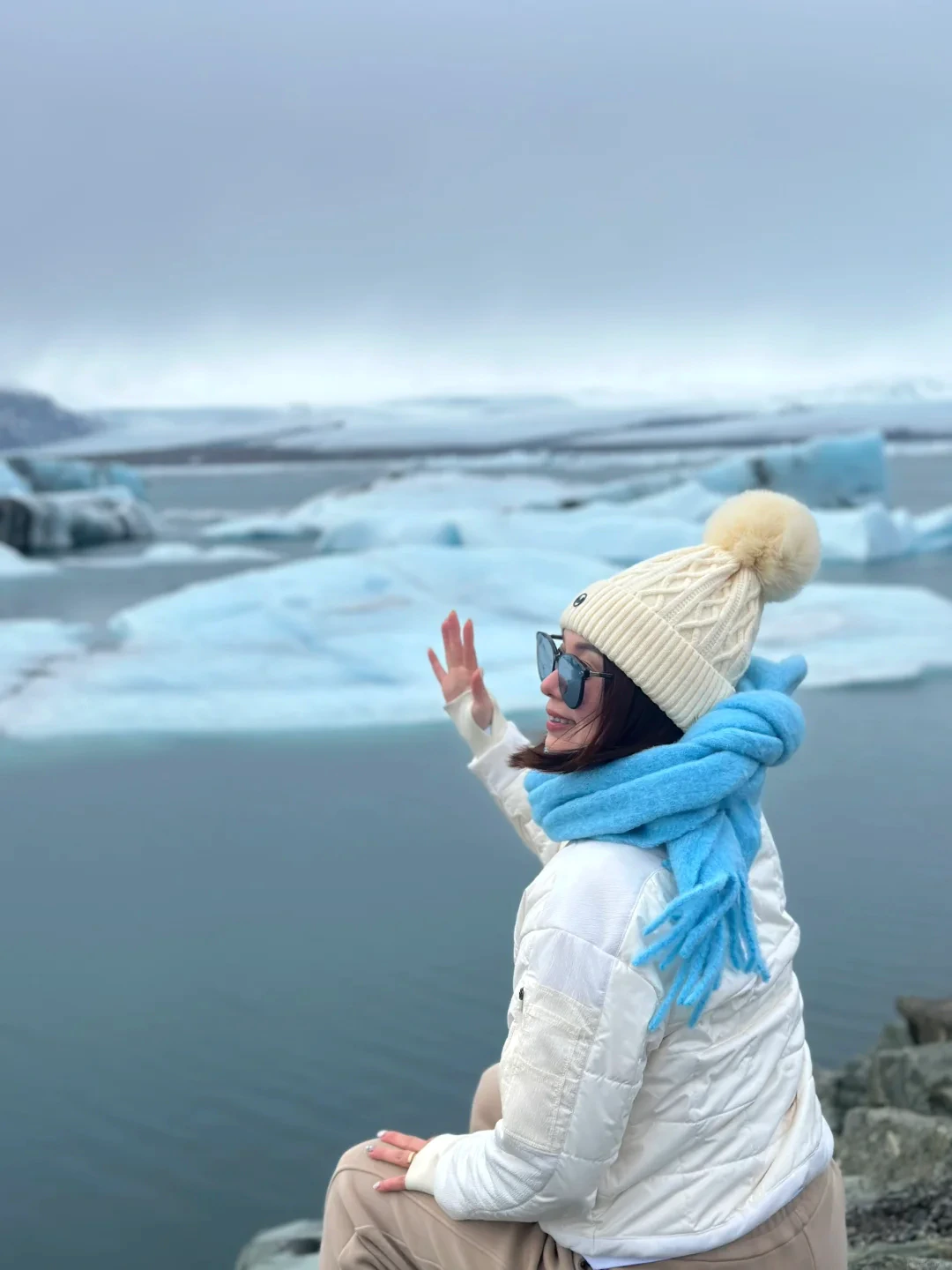 Alicia in winter white and vivid blue beside an Icelandic glacier lagoon