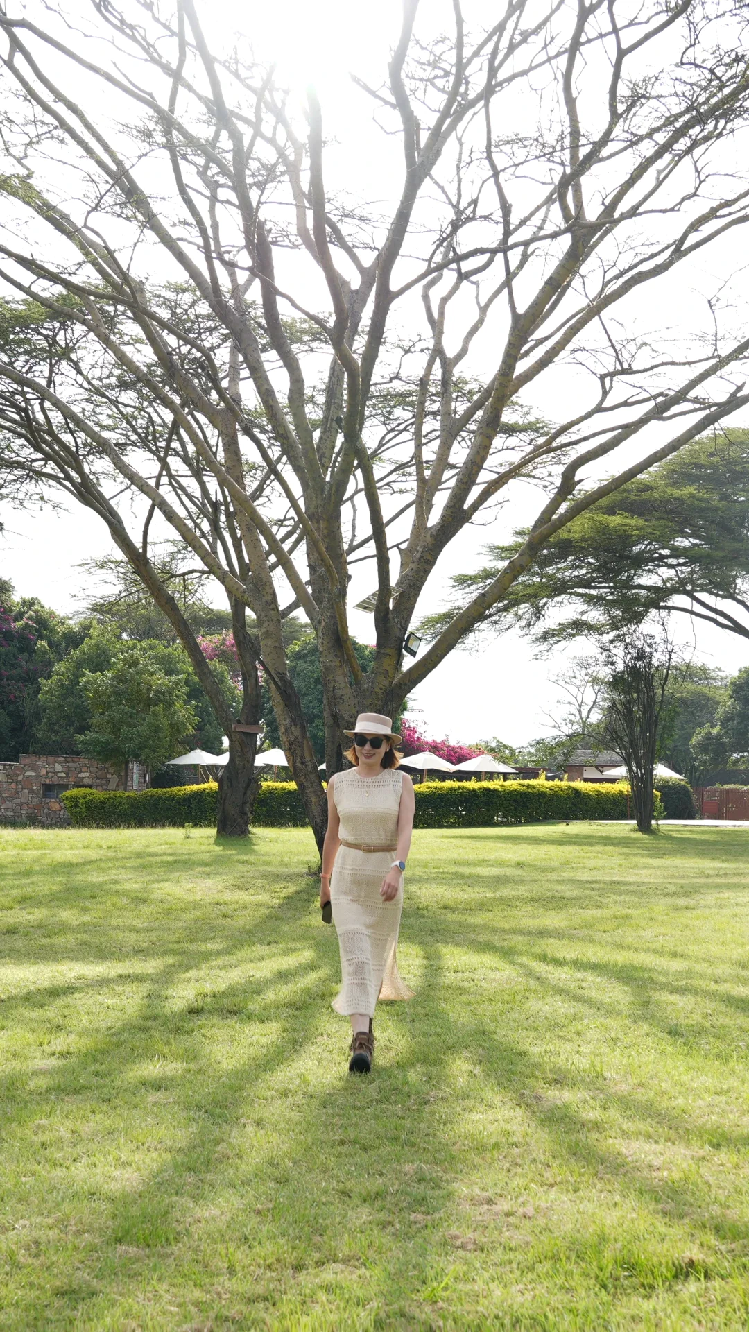 Alicia walking across a sunlit lawn in a long ivory knit dress