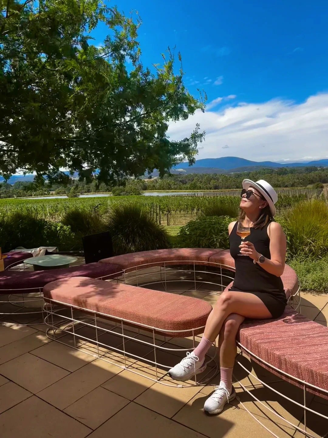 Alicia in a black dress and white hat seated at a Yarra Valley winery